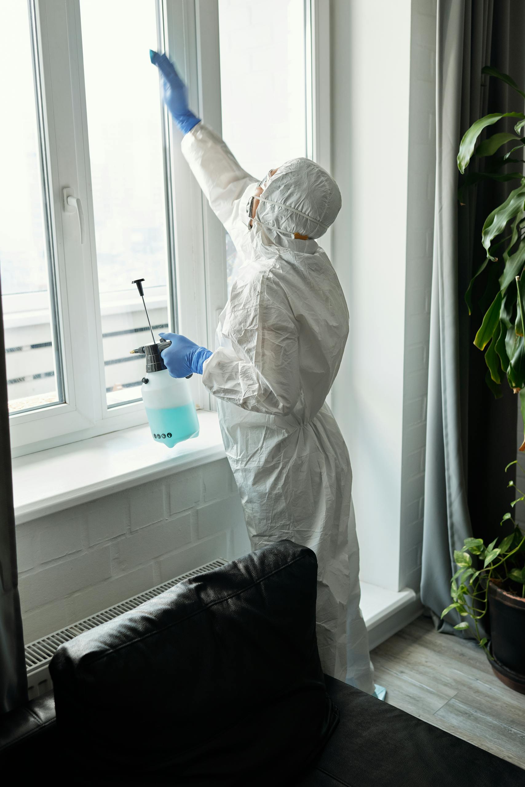 Person in full PPE cleaning an indoor glass window, ensures hygiene.
